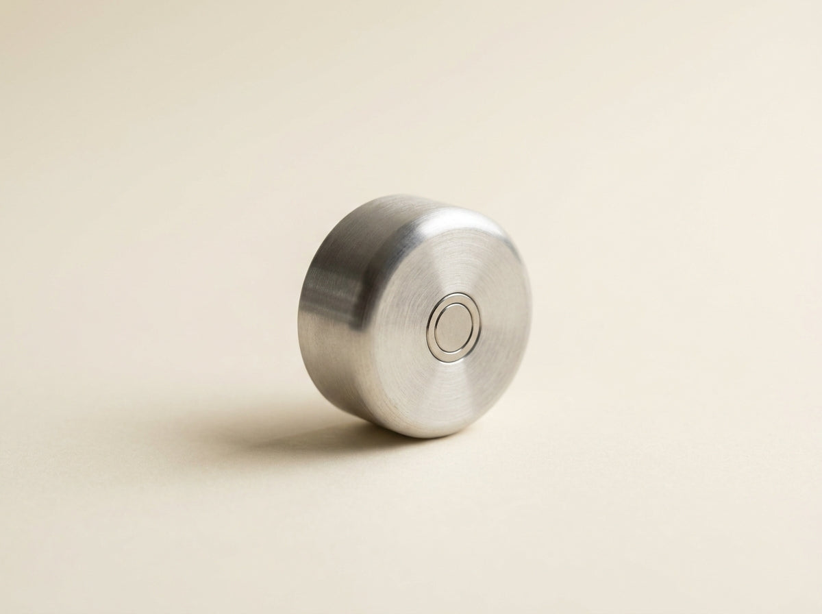 An early machined aluminum prototype of the Aura bottle cap on a cream surface